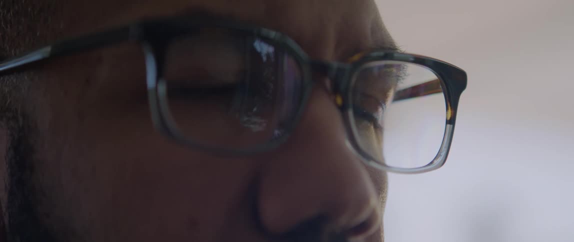 A man wearing glasses blinks a few times as he concentrates on reading