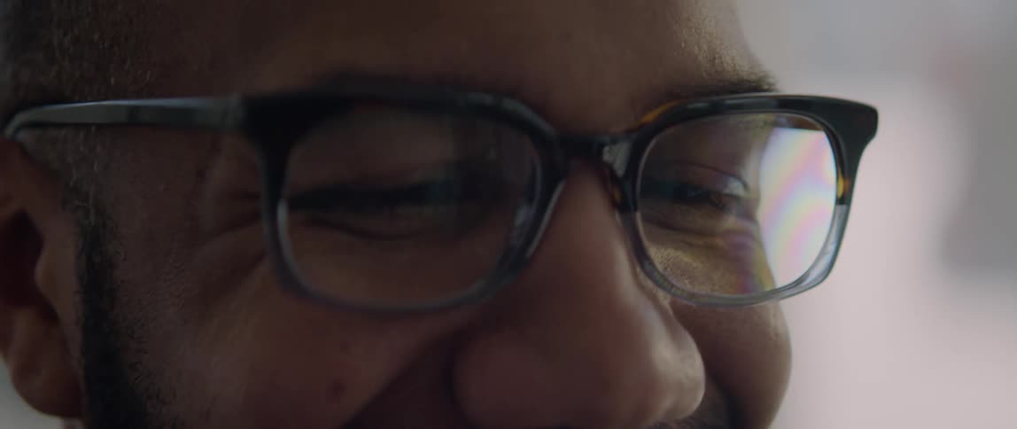 A man wearing glasses is smiling as he looks down