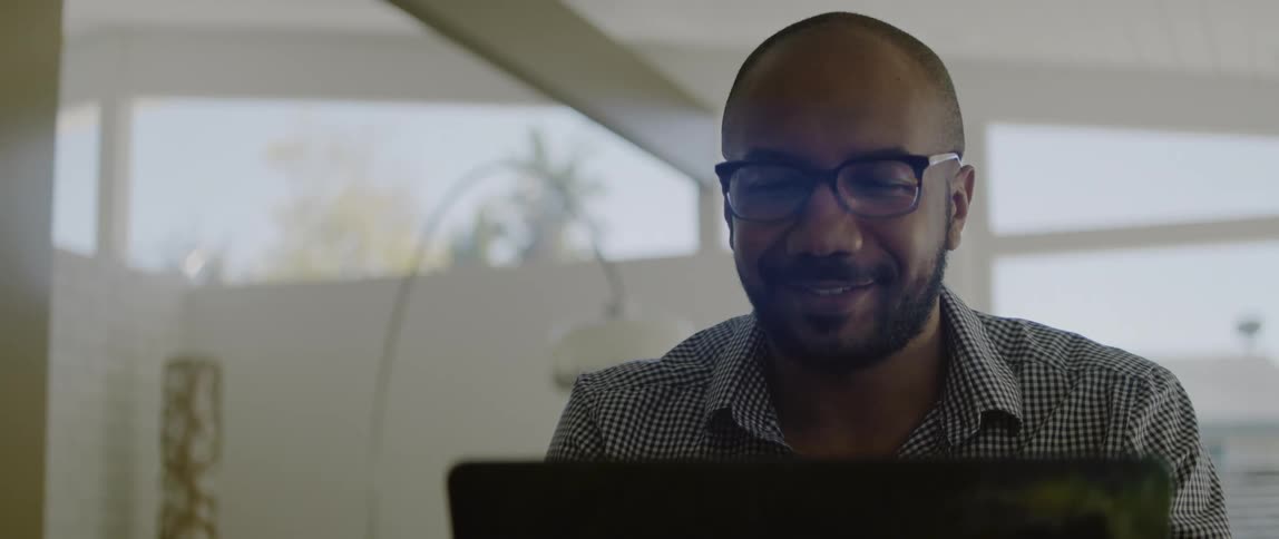 Man sits in front of laptop smiling and nodding while watching screen