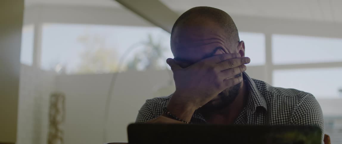 Man sitting in front of a laptop takes off his glasses and tiredly rubs his face
