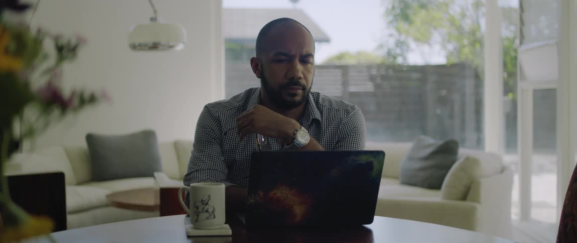 A man is sitting indoors and typing on his laptop