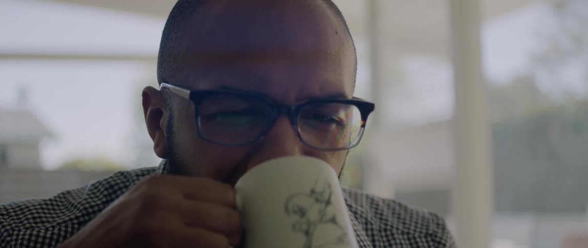 A man wearing glasses slowly takes a sip from his coffee cup