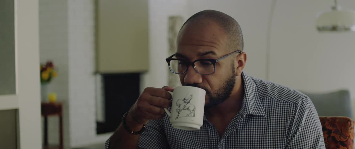 A man drinks coffee from a mug while sitting indoors during the day