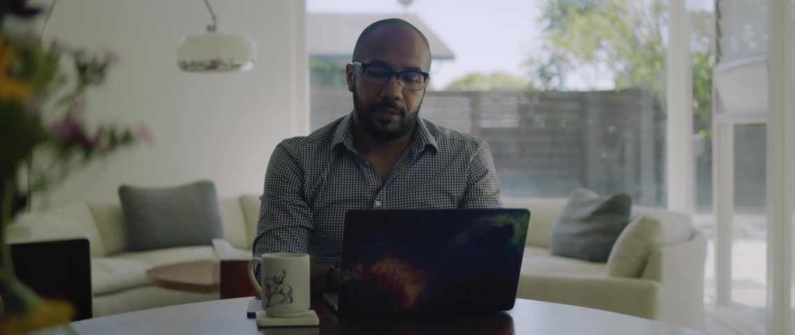 A man at home chats with someone on his laptop and then lets out a big sigh and takes his glasses off