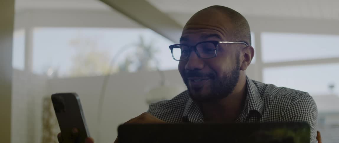 A man wearing glasses smiles while communicating via his smart phone