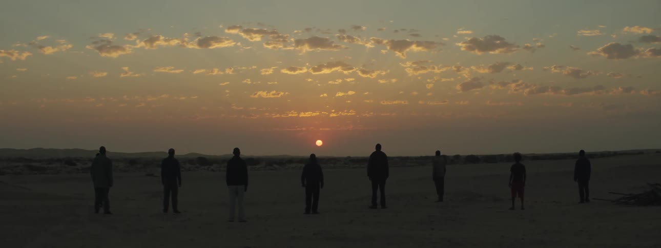 Eight people stand in a line outside watching the sunset on the horizon