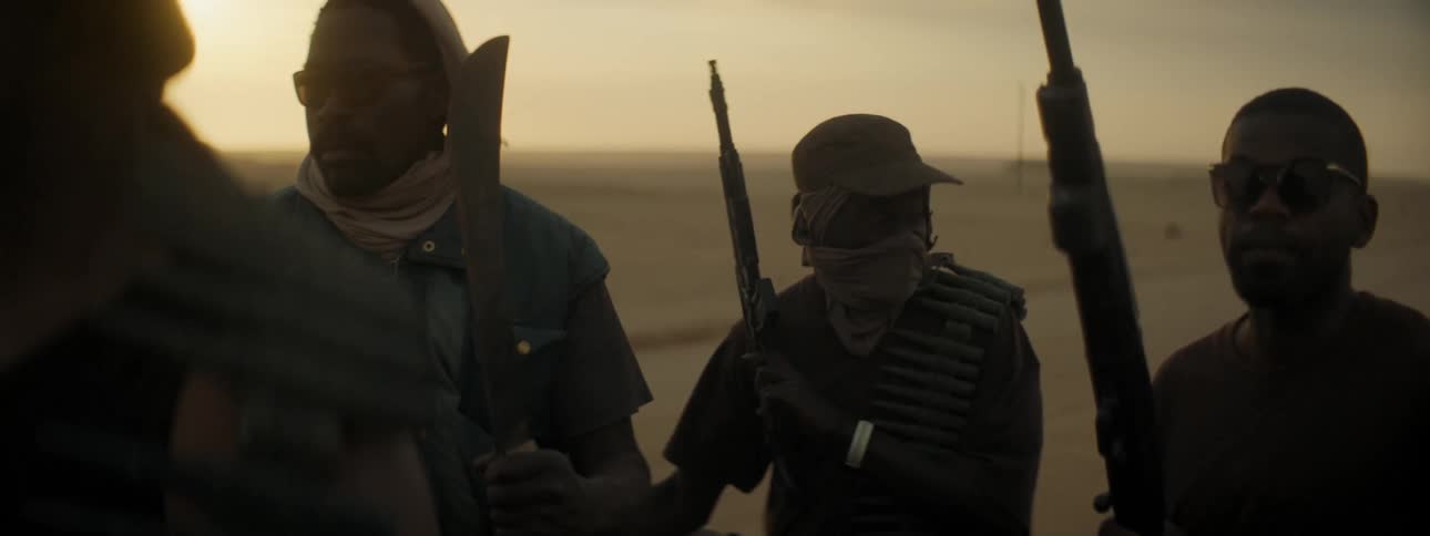 Four men driving across a field carrying guns and weapons