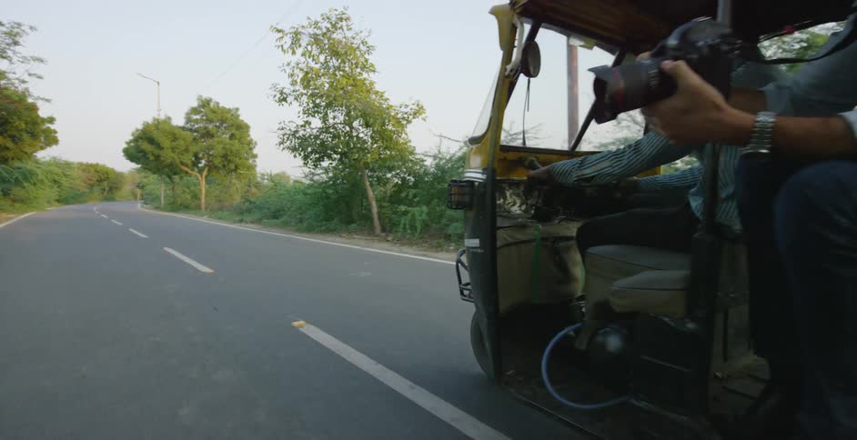 A photographer is riding in a tuk-tuk on a two lane street