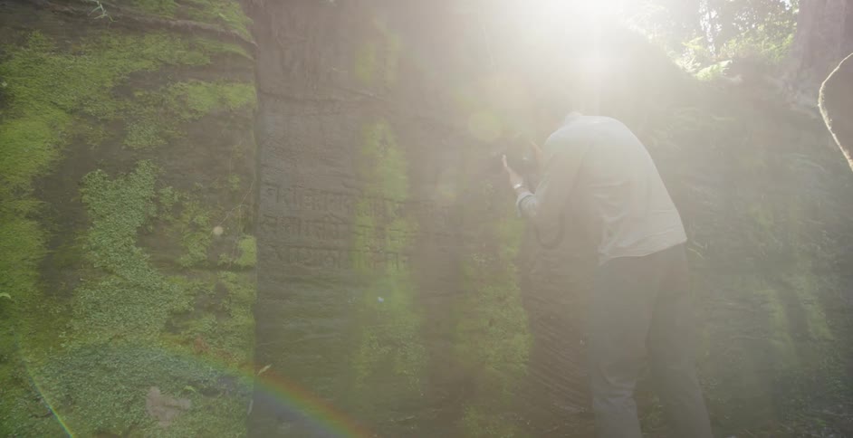 A man walks over to a stone wall with etchings and takes a photograph
