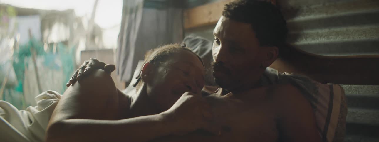 A woman rubs her husbands chest as they lie in bed together and he kisses her head