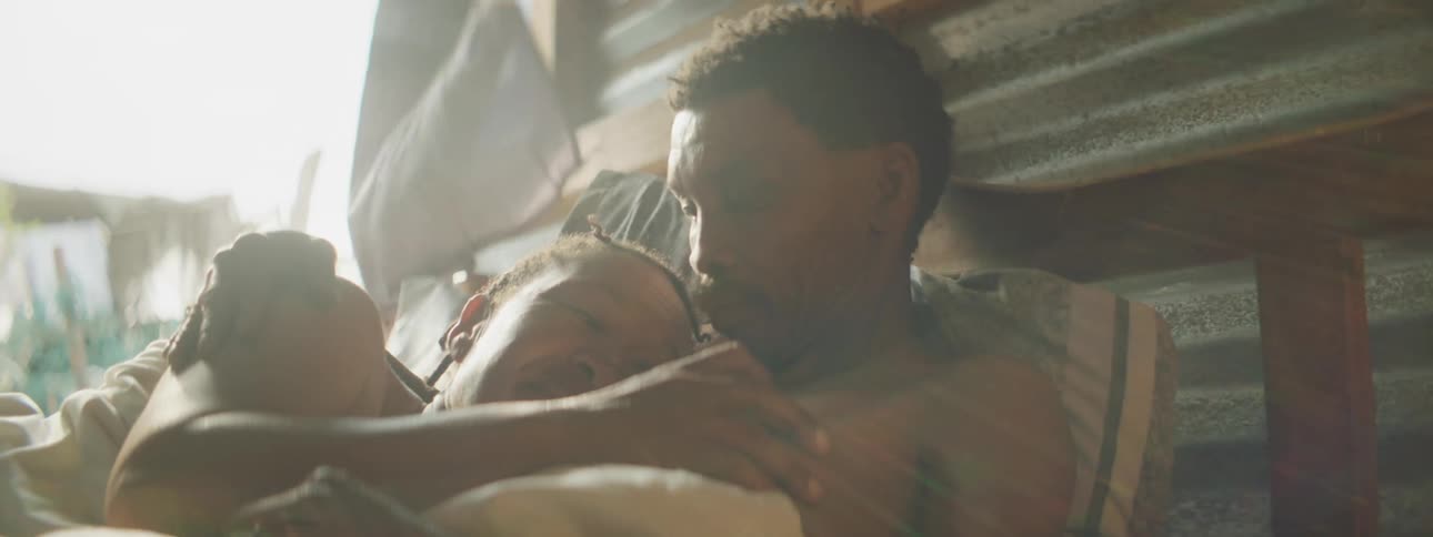 A man and a woman laying in bed and hugging with the sky and clouds in the background