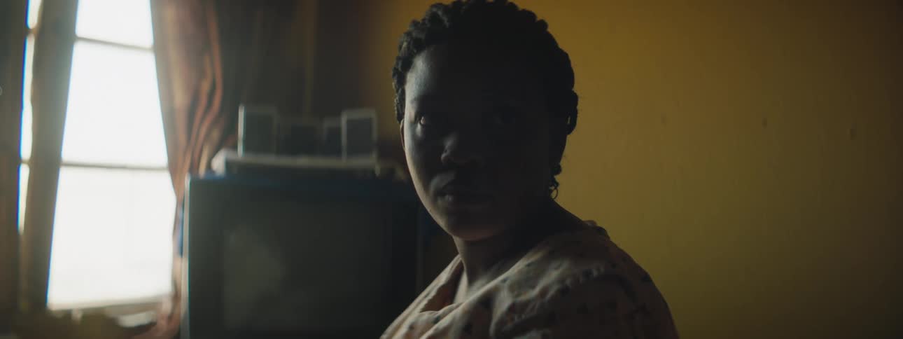 A woman in the living room of a house stares into the camera