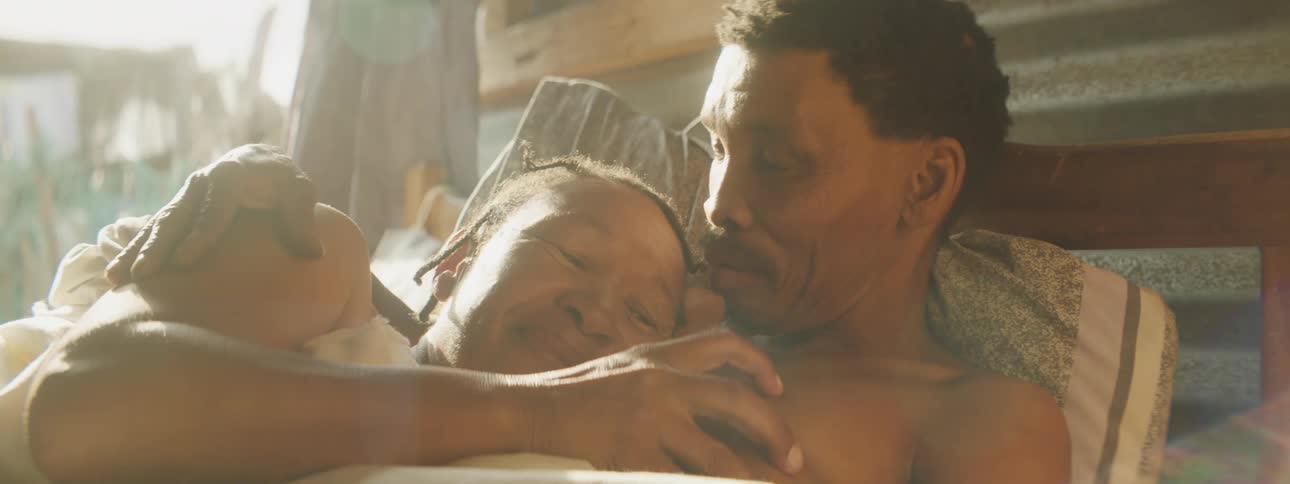 An older asian couple laying on a bench outside cuddling