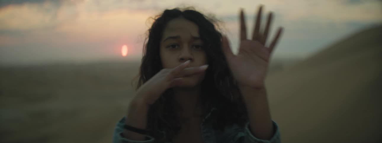 Girl waves her hands through the air standing in front of hills as sun rises on horizon