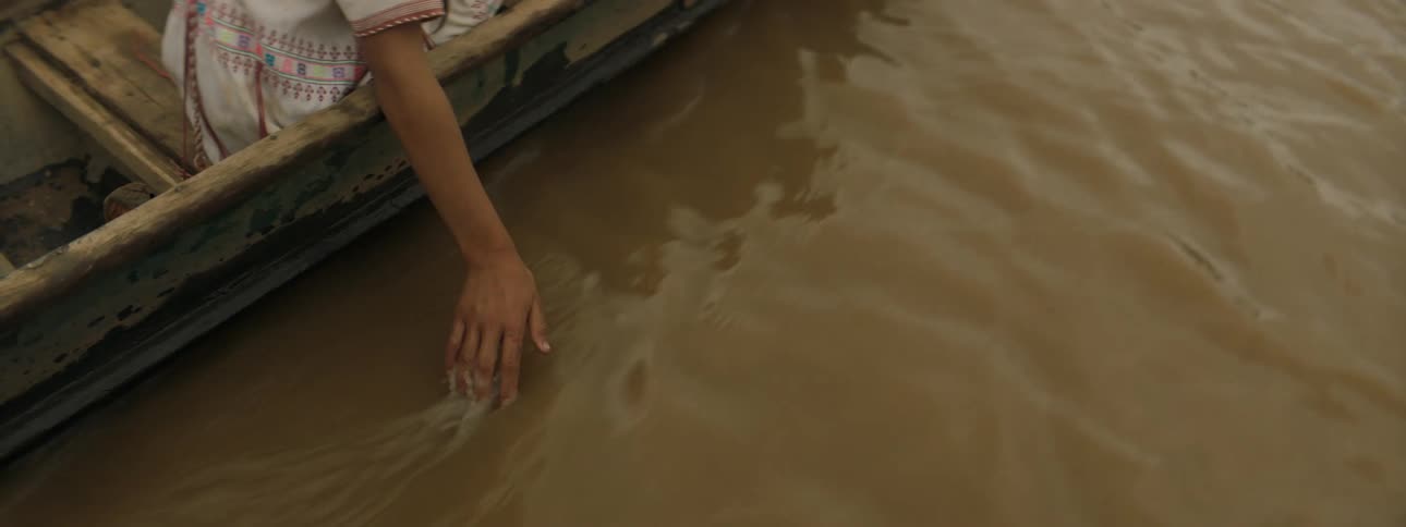 A person sits in a moving boat while dangling their hand into the water