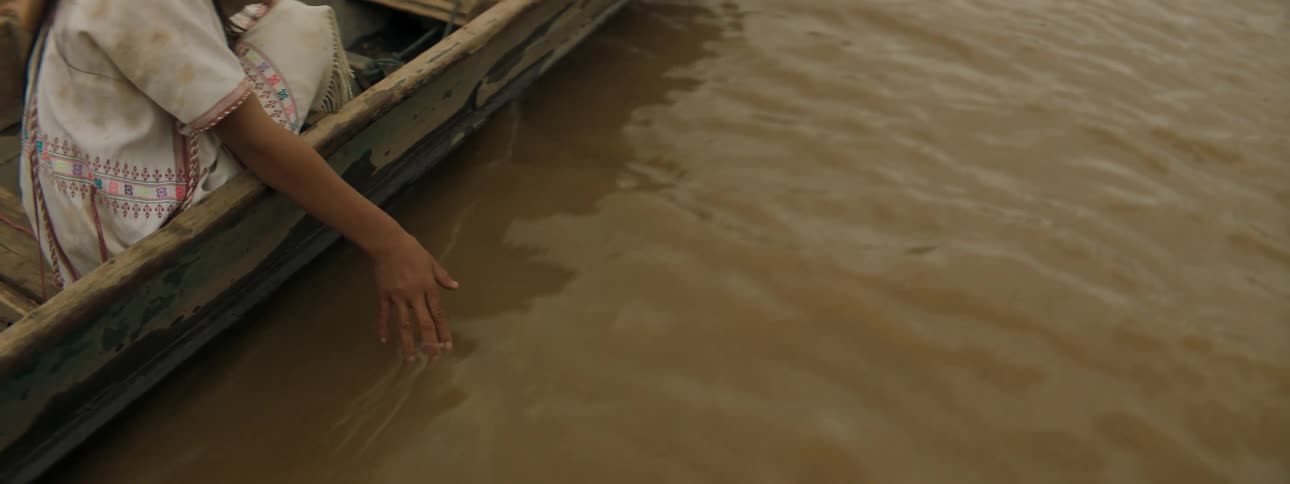 A girl sitting in a boat drags her hand through the water