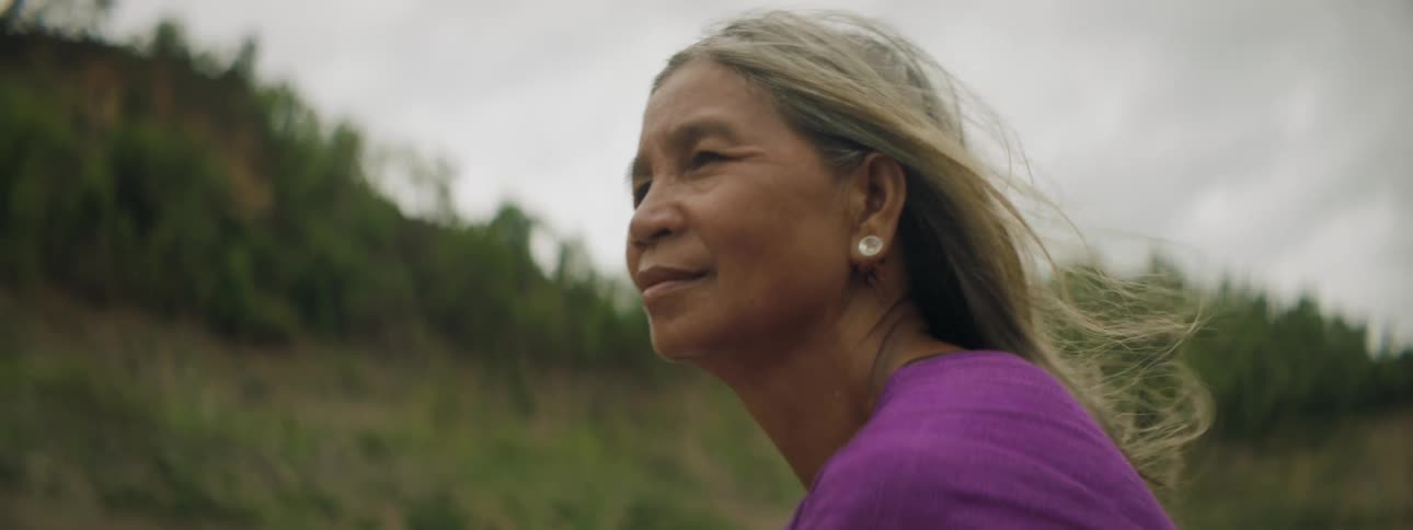 A native american woman sits outside rocking on a hillside with overcast weather