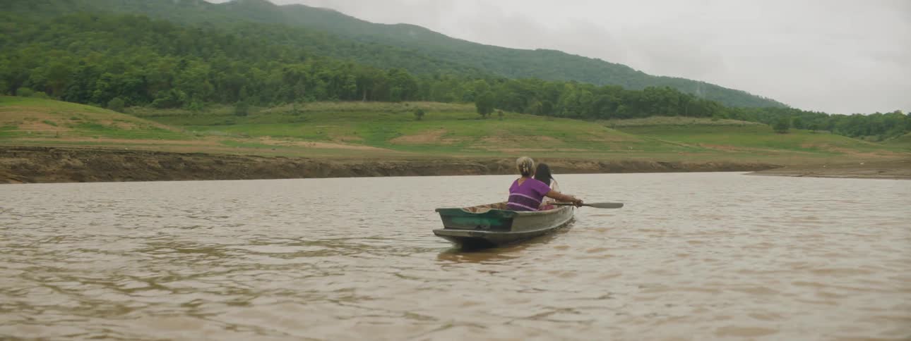 A woman rows a small boat in a lake with another person with her