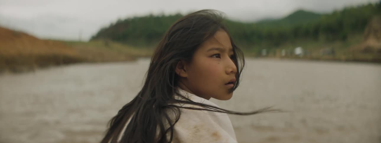 A girl gazes at her surroundings while sitting at the front of a boat as it travels down a river