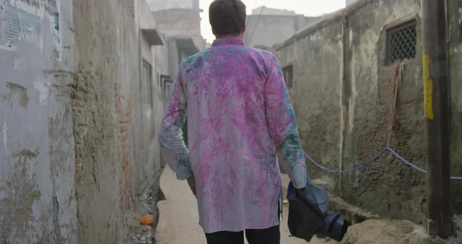A man covered in dyed powder walks through an alleyway