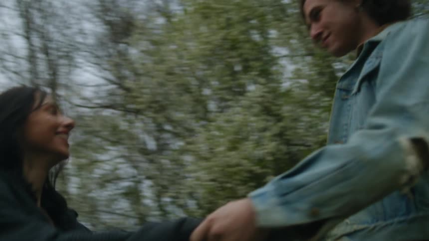 A young couple are outside laughing and dancing together near the woods