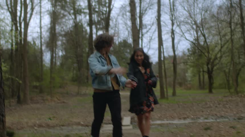 A teenage couple laugh as they run across a creek in the woods