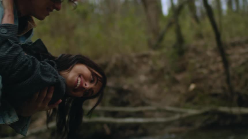 A teenage couple are outside laughing and dancing together in the woods