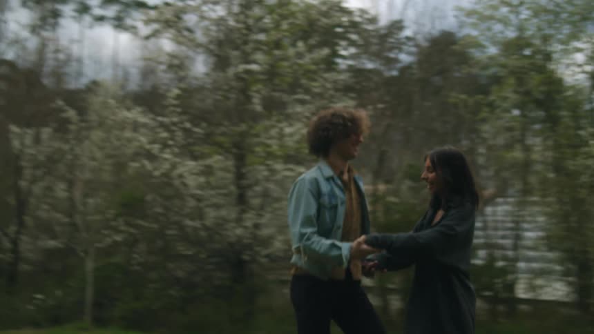 A man and woman run into a clearing and start dancing