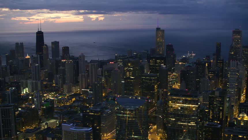 An aerial view of lit up office buildings in a city with the ocean in the background