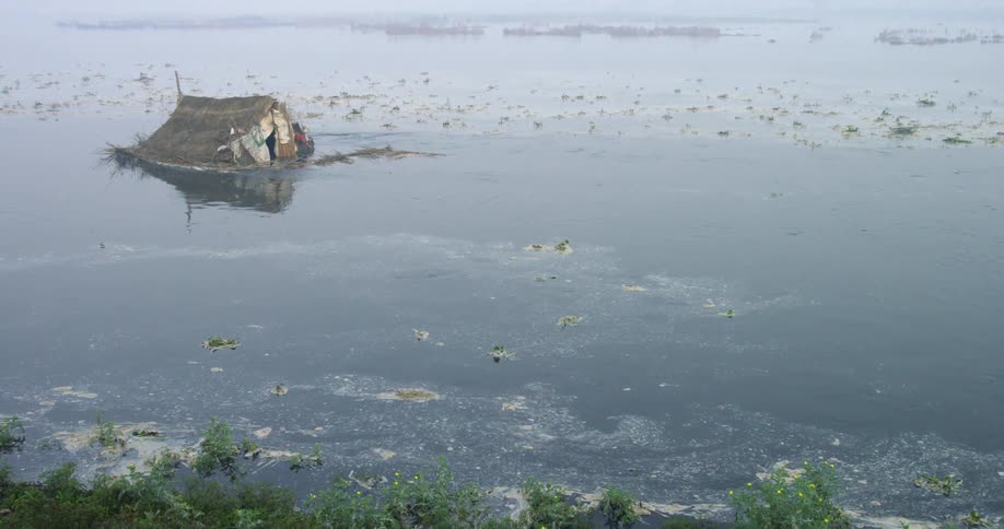 The water is murky with debris and a submerged house floating in it