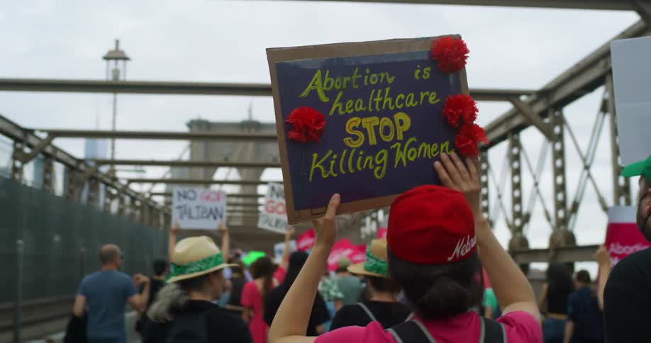 A group of protesters carry signs while marching across a bridge during the day