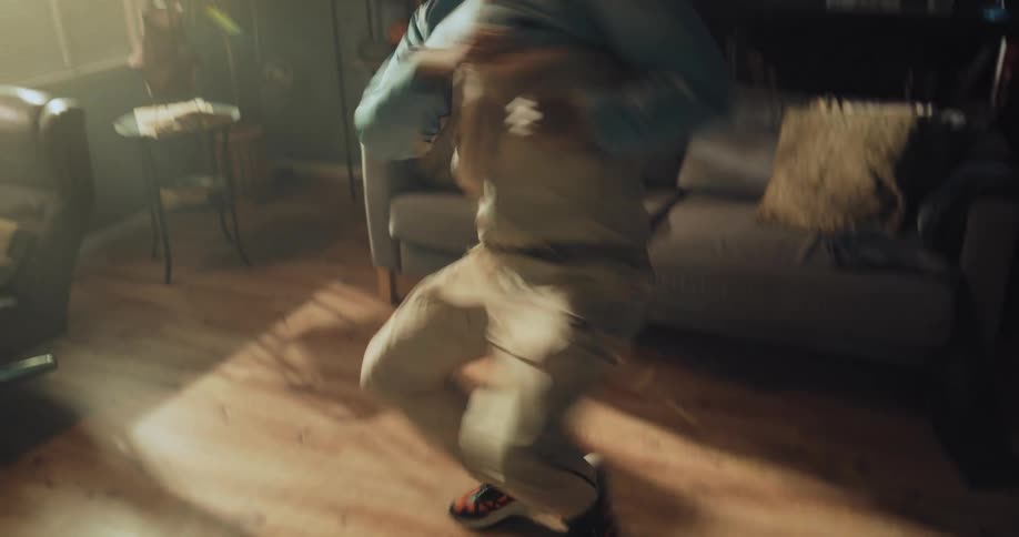 A teen break dances on the wood floor of his living room