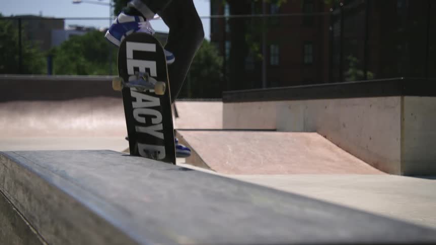 A teenage boy is riding his skateboard in a skateboard park and leaps in the air landing on a ledge where he is doing a wheelie