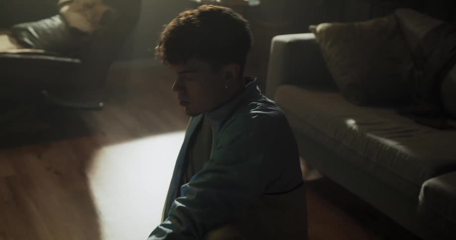 A teen scoots back onto the wooden floor and does leg stretches