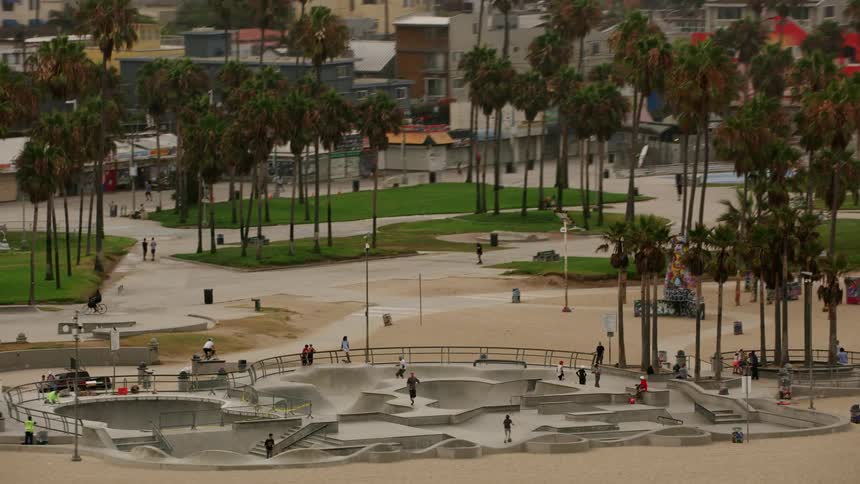People skate in a skate park on a beach in a city during the day