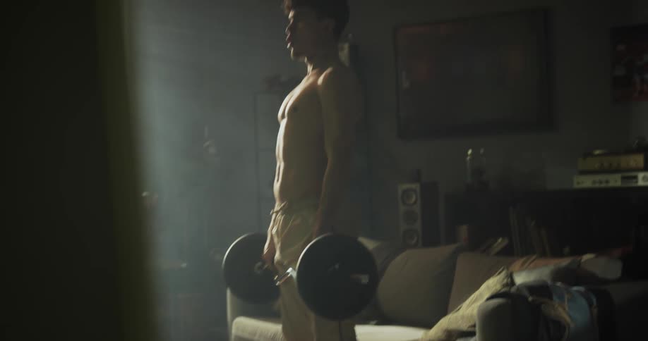 A teenage boy is standing in front of a couch working out with weights