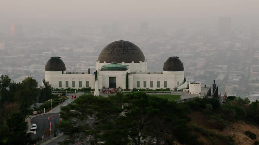 People walking the gardens at the griffith observatory with the los angeles skyline visible through the haze