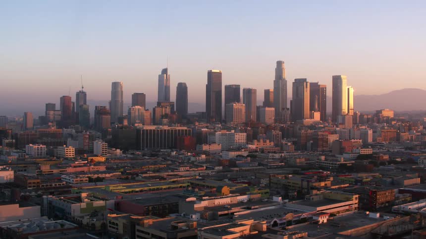 The los angeles city skyline with a silhouette of hills behind and sunlight reflecting on building facade