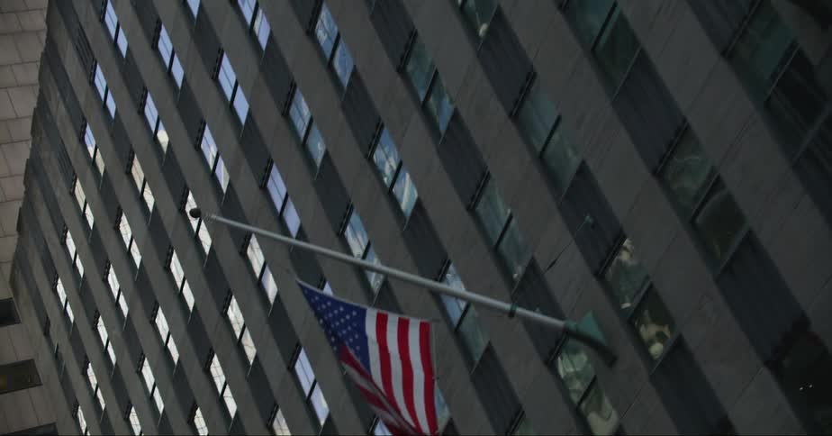 An american flag is hanging from a pole on the side of a tall building in a city
