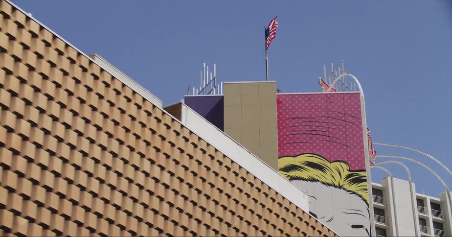 A mural of an old comic strip is painted on a building with an american flag flying on the top