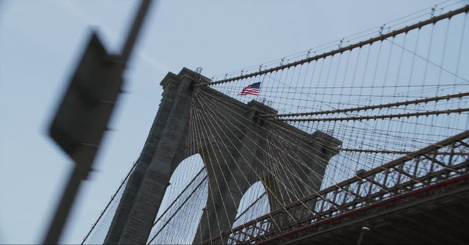 An american flag waves atop the tower of a large bridge during the day