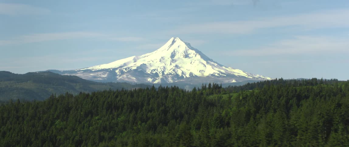 A tall ice covered volcano rises about mountains and farmland