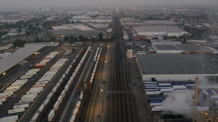 A large shipping hub is shown in a city with trains and semi trucks