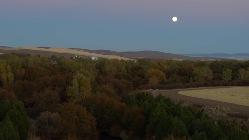 A full moon shines brightly in the sky over a farmland countryside in the evening