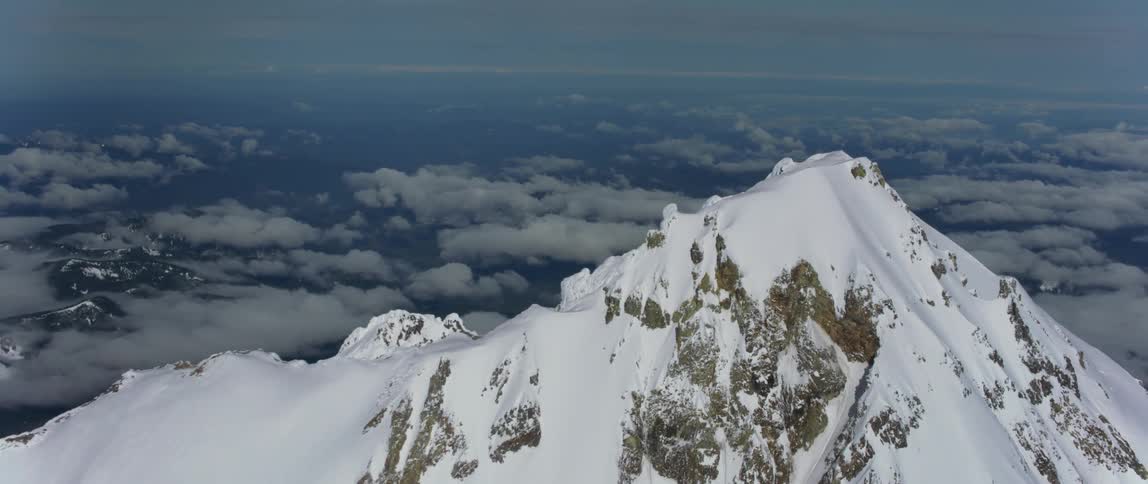 A snow covered mountain peak looms over a vast countryside during the day
