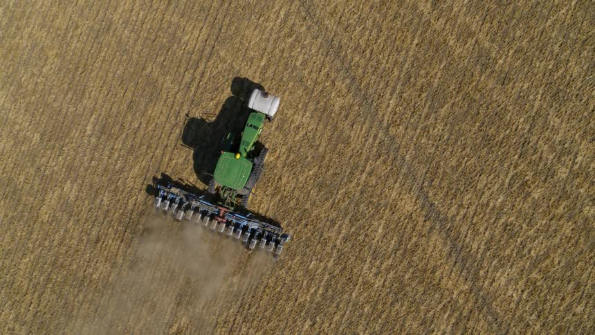 Birds eye view of a green tractor precision planting seeds on a freshly tilled farm field