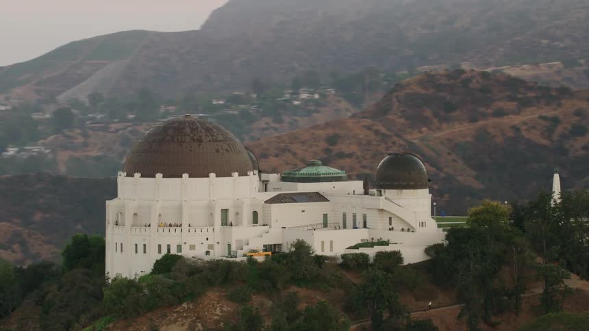 A domed observatory is on a hilltop overlooking a city surrounded by mountains