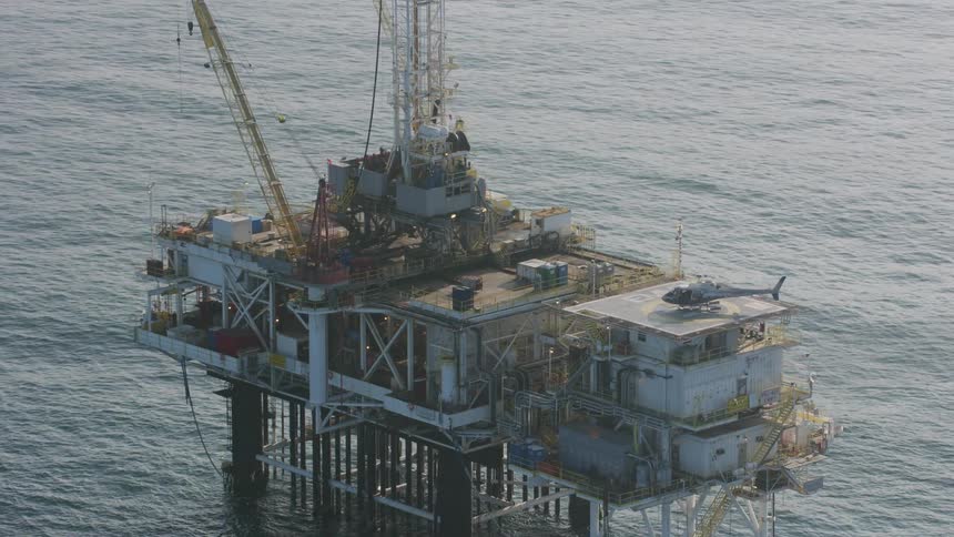 People exit a helicopter on the landing pad of an oil platform on the ocean during the day
