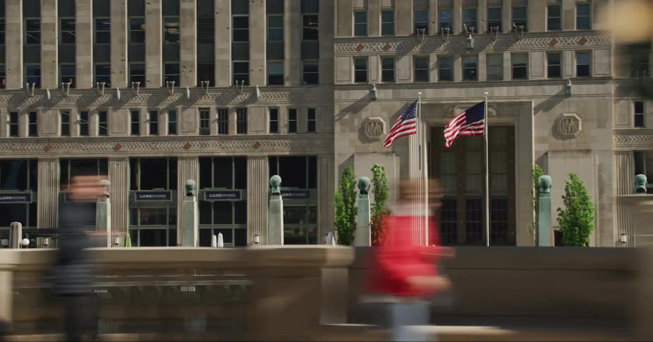 Two american flags on poles stand in front of a city building as traffic travels past