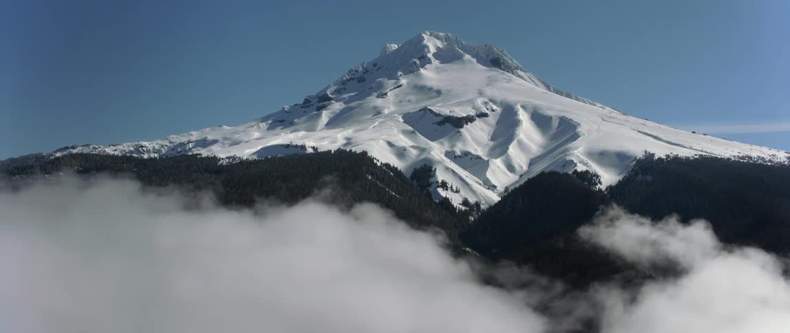 A snow capped mountain peak looms over a sea of clouds during the day